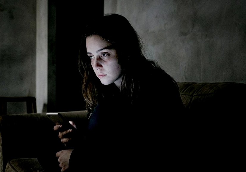 Pessoa sozinha olhando o celular em um ambiente escuro, representando a dificuldade de lidar com o silêncio e o tédio